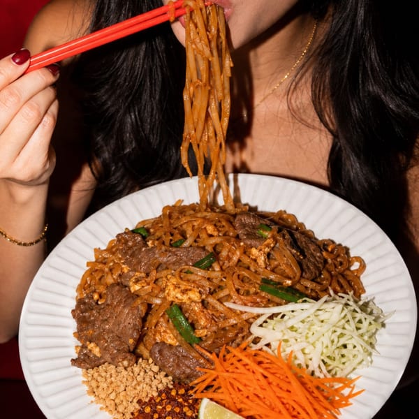 A person eating beef pad see ew with red chopsticks from a white plate.