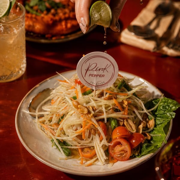 A hand squeezes lime juice over a plate of Pink Pepper's papaya salad with peanuts and tomatoes.