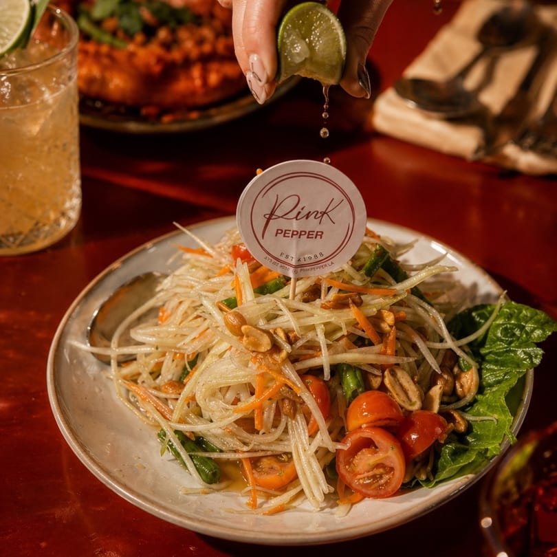A hand squeezes lime juice over a plate of Pink Pepper's papaya salad with peanuts and tomatoes.