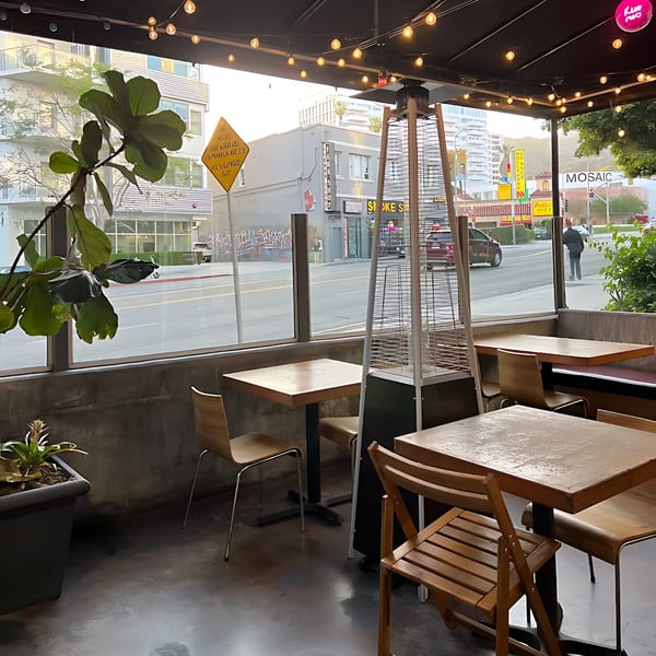 Outdoor patio seating at Pink Pepper, with wooden tables and chairs, overlooking a city street.