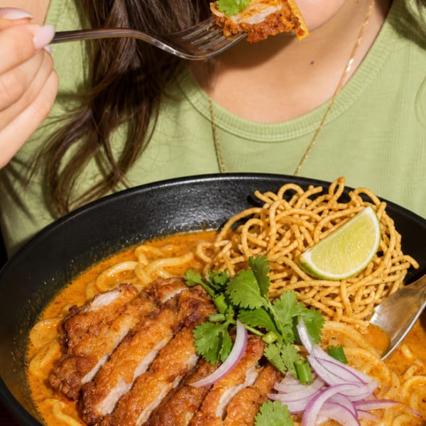 A person eating a bowl of Khao Soi with crispy chicken, noodles, and lime.