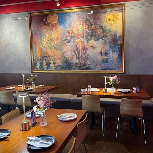 Pink Pepper's dining room with wooden tables, chairs, and a large colorful Thai-inspired painting.