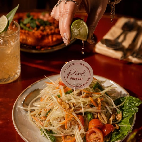 A hand squeezes lime over a fresh papaya salad with peanuts, tomatoes, and green beans.