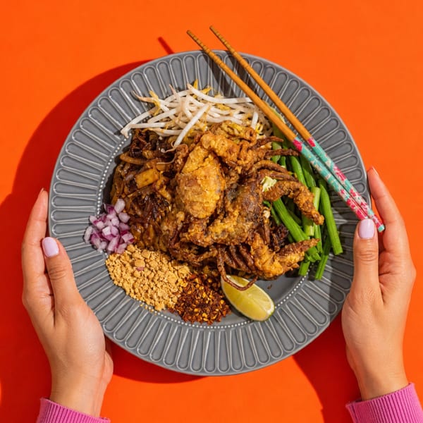 Hands holding a plate of Pad See Ew with crispy soft-shell crab, bean sprouts, and green beans.