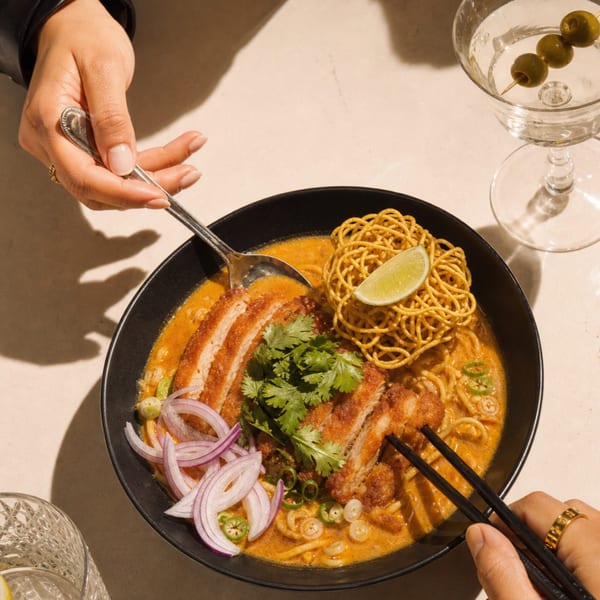 Two people sharing a bowl of katsu curry ramen with a martini and water glass.
