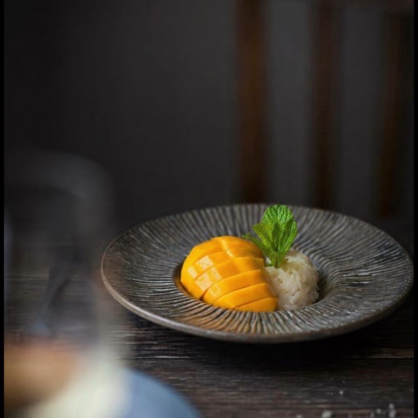 Mango sticky rice dessert with fresh mint on a textured gray plate.
