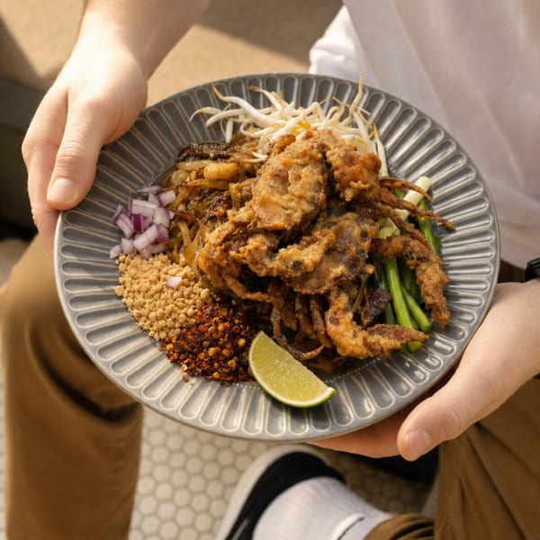 Hands holding a plate of Pad See Ew with crispy soft-shell crab, bean sprouts, and lime.